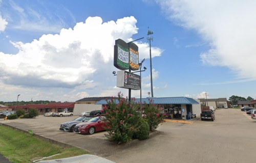 A storefront with a blue roof and signage, surrounded by parked cars under a partly cloudy sky.