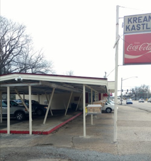 A small building with a sign reading "Kream Kastle," featuring a covered parking area and nearby street view.