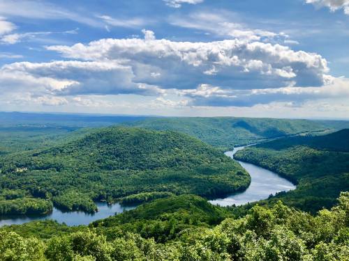 A scenic view of lush green hills and a winding river under a blue sky with fluffy clouds.