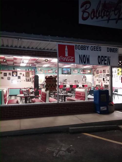 A diner named Bobby Gee's, brightly lit with red and white decor, featuring tables and vintage photos on the walls.