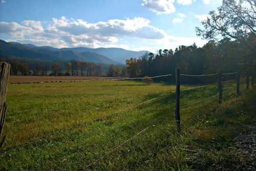 A scenic view of a grassy field with mountains in the background under a partly cloudy sky.