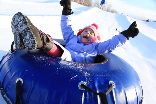 A joyful child in a blue snow tube, laughing and having fun while sliding down a snowy hill.