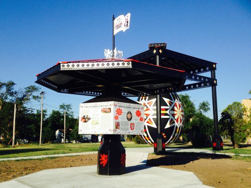 A colorful, decorative pavilion with a large ornament, set against a clear blue sky and green landscape.