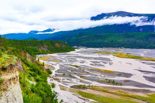 A scenic view of a winding river surrounded by lush green mountains and cloudy skies.