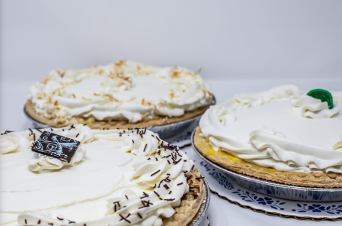 Three cream-topped pies with decorative swirls and chocolate accents, set against a plain background.