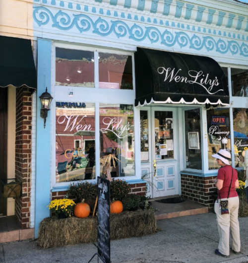 A woman stands outside Wen Lily's shop, featuring a blue facade, pumpkins, and fall decorations.