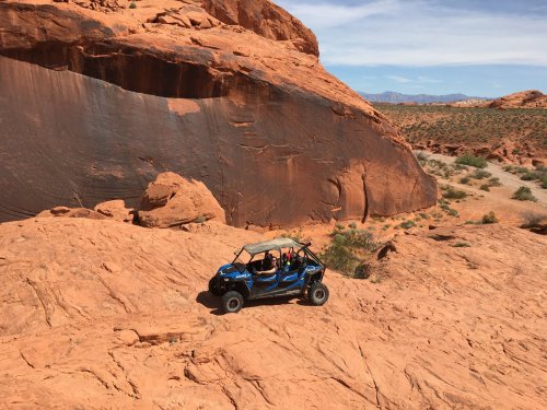 A blue off-road vehicle navigating rocky terrain in a desert landscape with red rock formations.