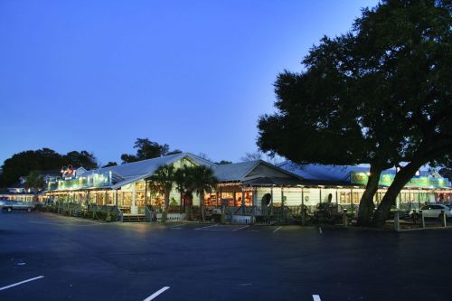 A row of shops illuminated at dusk, surrounded by trees and a parking lot.