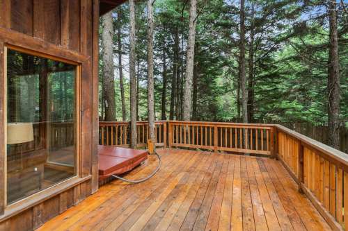 Wooden deck with a hot tub, surrounded by tall trees and greenery, creating a serene outdoor space.