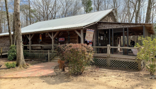 A rustic wooden building with a metal roof, surrounded by trees and a path leading to the entrance.
