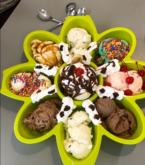 A colorful ice cream platter with various flavors, topped with sprinkles, cherries, and whipped cream, arranged in a flower shape.