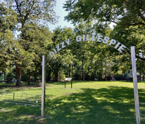 Archway sign reading "Dizzy Gillespie" in a green park surrounded by trees.