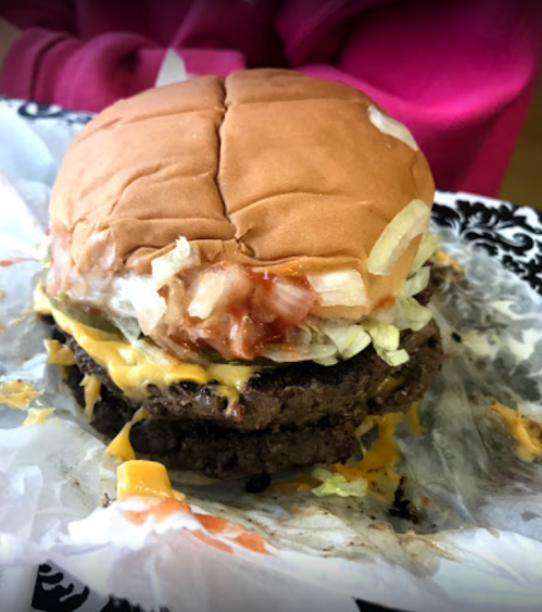 A close-up of a double cheeseburger with lettuce, tomato, and ketchup on a paper plate.
