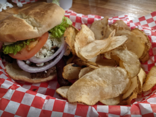 A juicy burger with lettuce, tomato, and onion, served with a side of crispy potato chips in a red-checkered basket.