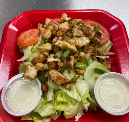 A colorful salad with grilled chicken, lettuce, tomatoes, green peppers, and two cups of dressing on a red tray.