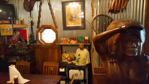 A rustic interior featuring wooden decor, a mannequin, and vintage items against a corrugated metal wall.