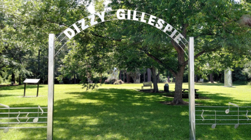 Archway reading "Dizzy Gillespie" in a green park with trees and benches in the background.