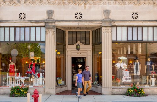 A couple walks past a storefront with colorful clothing displays and a vintage architectural facade.