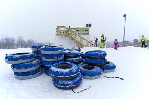 A stack of blue snow tubes on a snowy hill, with people in winter gear near a wooden observation deck.