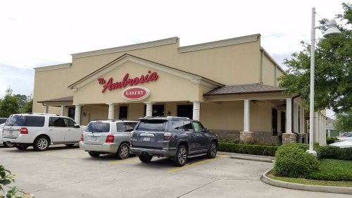 Exterior view of Ambrosia Bakery with several parked cars in the foreground and a clear sky above.
