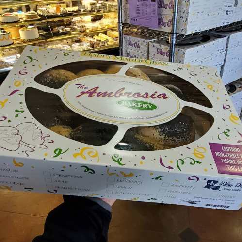 A hand holding a large box of assorted pastries from Ambrosia Bakery, decorated with colorful confetti and text.