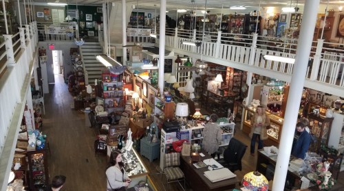 A spacious antique store filled with various items, showcasing multiple levels and shoppers browsing among the displays.