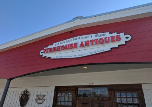 Sign for "Firehouse Antiques" on a red building, featuring details about hours and collectibles available.