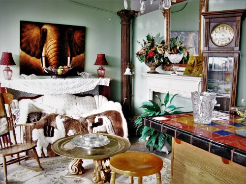 Cozy living room with an elephant painting, floral decor, a clock, and a mix of vintage furniture and textures.