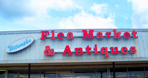 Sign for "Wetumpka Flea Market & Antiques" against a blue sky with clouds.