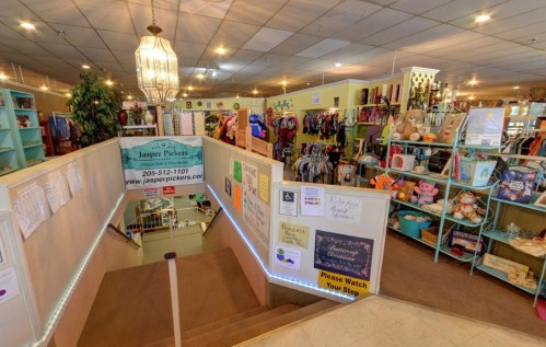 A colorful store interior with clothing racks, toys, and decor, viewed from the top of a staircase.
