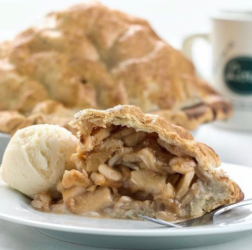A slice of apple pie with a scoop of vanilla ice cream on a plate, with a whole pie in the background.