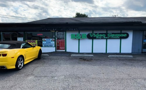 A yellow convertible parked outside B&B Video Games store, featuring a sign for buying, selling, and trading video games.