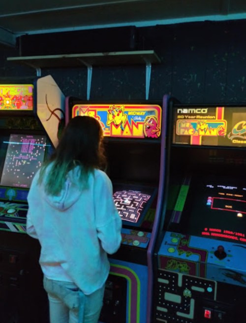 A person playing a classic arcade game, Ms. Pac-Man, in a dimly lit arcade filled with retro machines.
