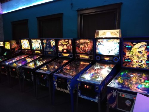 A row of colorful pinball machines illuminated in a dimly lit arcade.