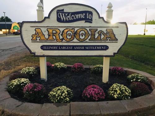 Welcome sign for Argola, Illinois, featuring flowers and stating it's the largest Amish settlement in the state.
