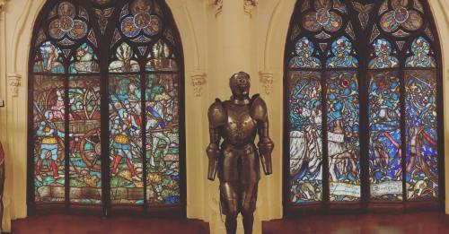 Stained glass windows depicting knights and a suit of armor in a historic setting.