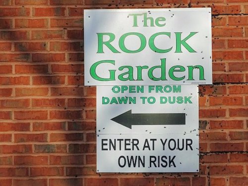 Sign for "The Rock Garden," open from dawn to dusk, with an arrow pointing left and a warning to enter at your own risk.
