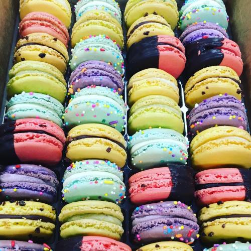 A colorful assortment of macarons in various flavors, arranged neatly in a box, some with chocolate and sprinkles.