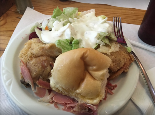 A plate with fried chicken, a sandwich bun, and a salad topped with creamy dressing.