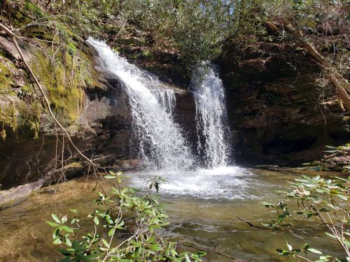 A serene waterfall cascading into a clear pool, surrounded by lush greenery and rocky terrain.