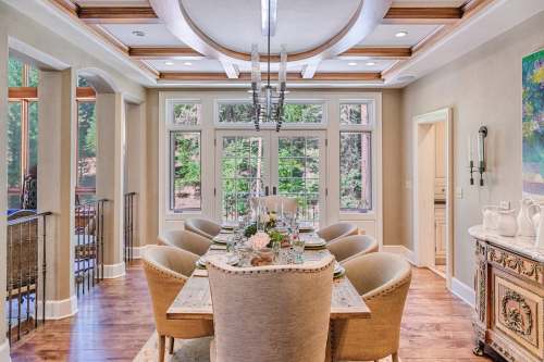 Elegant dining room with a long table set for a meal, large windows, and stylish decor, surrounded by greenery.