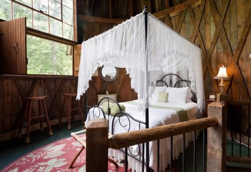 Cozy bedroom with a canopy bed, wooden walls, large windows, and a warm, inviting atmosphere.