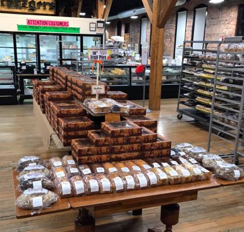 A bakery display featuring stacked boxes of fruit pies and assorted muffins on a wooden table in a rustic shop.