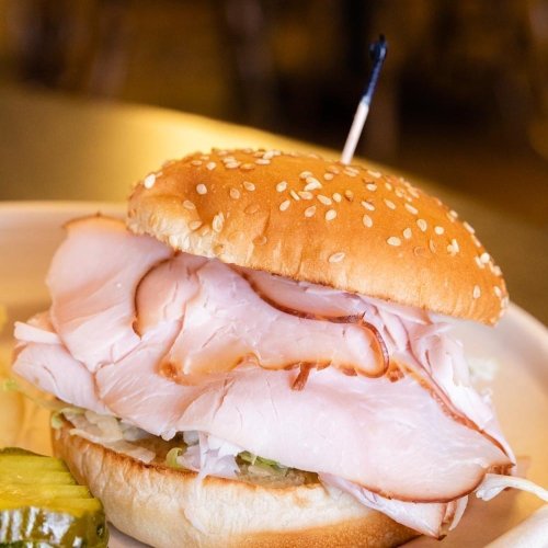 A sesame seed bun filled with layers of turkey, lettuce, and a pickle on the side.