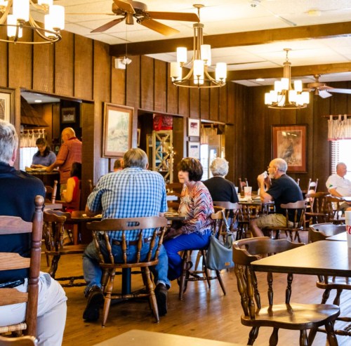 A cozy restaurant interior with wooden decor, featuring diners seated at tables and chatting in a relaxed atmosphere.