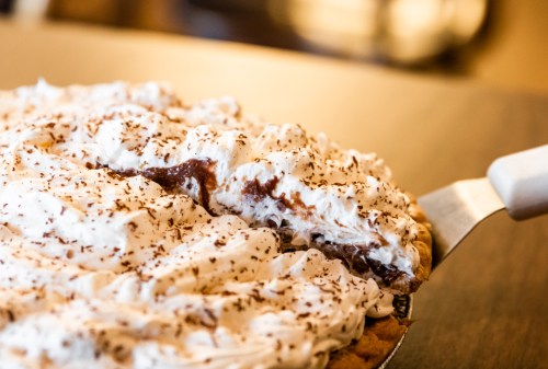 A slice of chocolate cream pie being served, topped with whipped cream and chocolate shavings.
