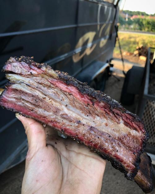A hand holding a thick slice of smoked brisket, showcasing its juicy layers and charred exterior.