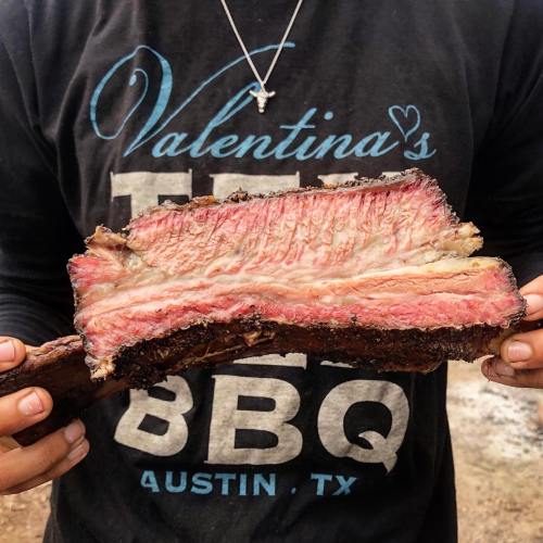 A person holds a large, juicy piece of smoked brisket, showcasing its pink interior and charred exterior.