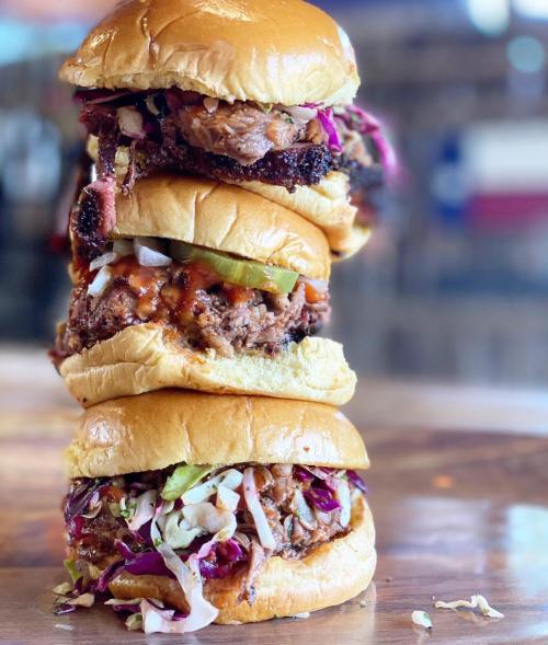 A towering stack of three delicious burgers, each layered with meat, pickles, and coleslaw on soft buns.