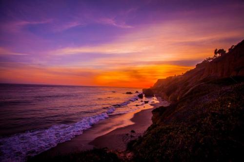 A vibrant sunset over a coastal beach, with waves gently lapping at the shore and colorful skies.